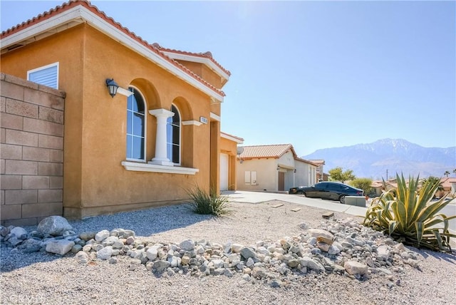 view of home's exterior with concrete driveway, a tile roof, a mountain view, and stucco siding