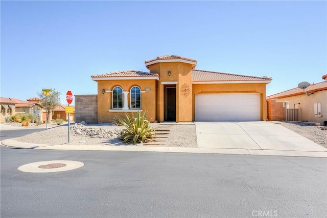 mediterranean / spanish-style home with concrete driveway, an attached garage, a tiled roof, and stucco siding