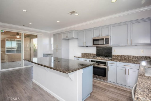 kitchen featuring light wood-style flooring, stainless steel appliances, visible vents, ornamental molding, and dark stone countertops