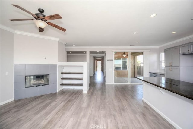 unfurnished living room with ornamental molding, a tiled fireplace, light wood-style flooring, and baseboards