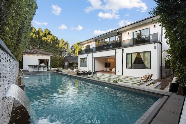 rear view of property with a balcony, a patio area, an outdoor pool, and stucco siding