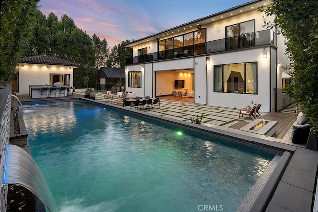 rear view of property featuring an outdoor pool, a balcony, outdoor dry bar, a patio area, and stucco siding