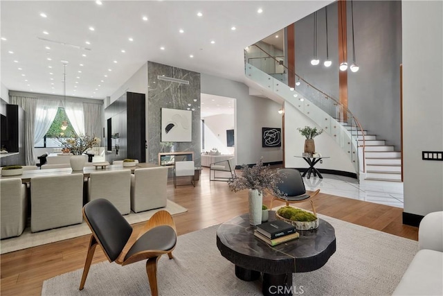 living area featuring a towering ceiling, a premium fireplace, stairway, wood finished floors, and recessed lighting