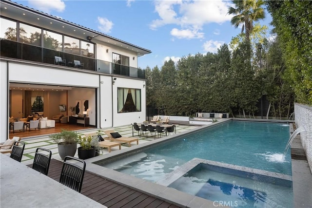 back of house with a garage, a balcony, a patio area, a pool with connected hot tub, and an outdoor living space