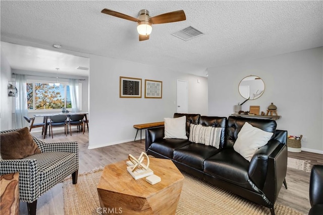 living area with light wood finished floors, visible vents, a textured ceiling, and ceiling fan with notable chandelier