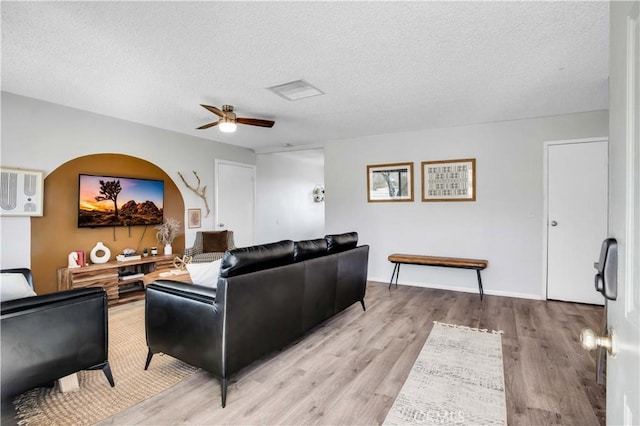 living room featuring baseboards, visible vents, a ceiling fan, a textured ceiling, and light wood-type flooring