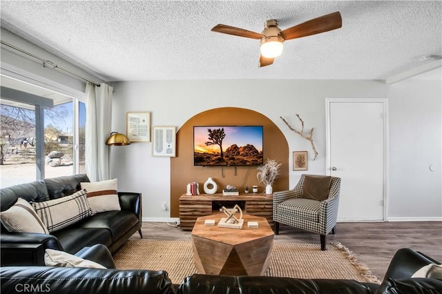 living room with ceiling fan, a textured ceiling, baseboards, and wood finished floors