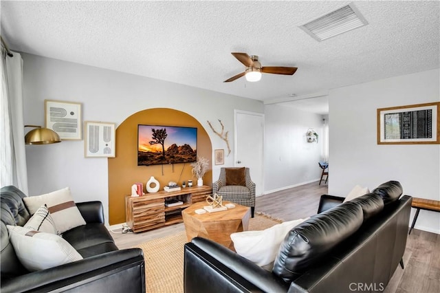 living area with a textured ceiling, wood finished floors, visible vents, and a ceiling fan