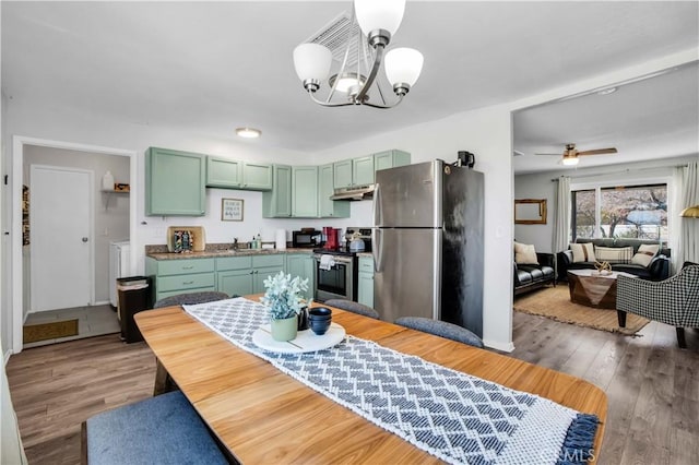 kitchen with appliances with stainless steel finishes, wood finished floors, under cabinet range hood, green cabinets, and a sink