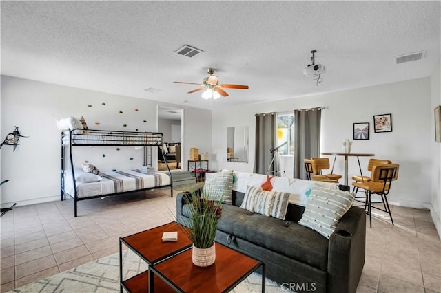 living room featuring light tile patterned floors, ceiling fan, visible vents, and a textured ceiling