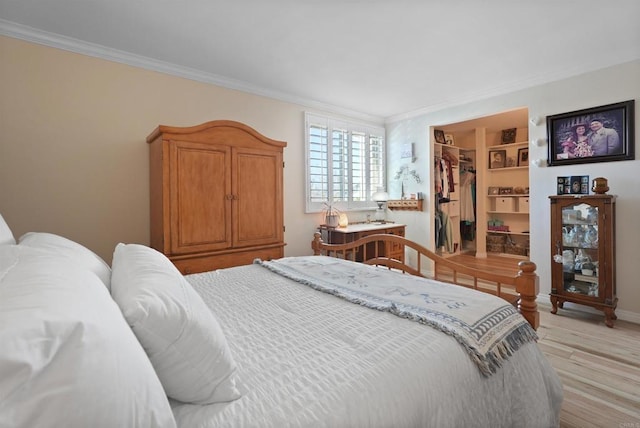 bedroom featuring light wood-style floors, a closet, crown molding, and a spacious closet