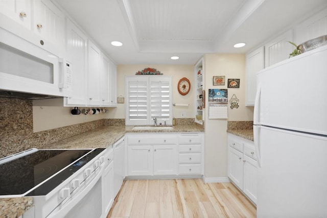 kitchen featuring white appliances, a sink, white cabinetry, light wood-style floors, and a tray ceiling