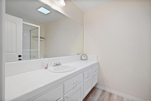 bathroom featuring a shower with shower door, vanity, baseboards, and wood finished floors