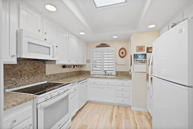 kitchen featuring white appliances, light wood finished floors, white cabinets, a tray ceiling, and a sink