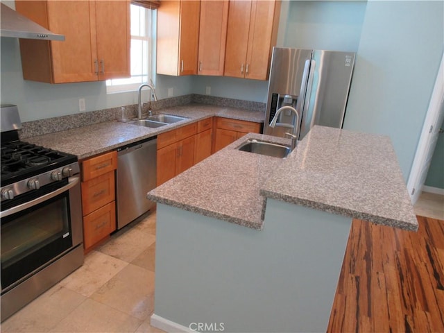 kitchen with stainless steel appliances, a sink, under cabinet range hood, and a center island with sink