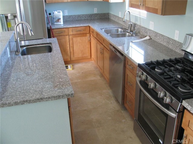 kitchen featuring appliances with stainless steel finishes, brown cabinets, a sink, and light stone countertops