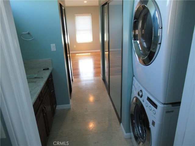 clothes washing area with stacked washer and dryer, baseboards, and cabinet space