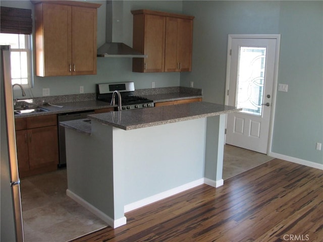 kitchen featuring appliances with stainless steel finishes, light wood-style floors, a sink, wall chimney range hood, and an island with sink