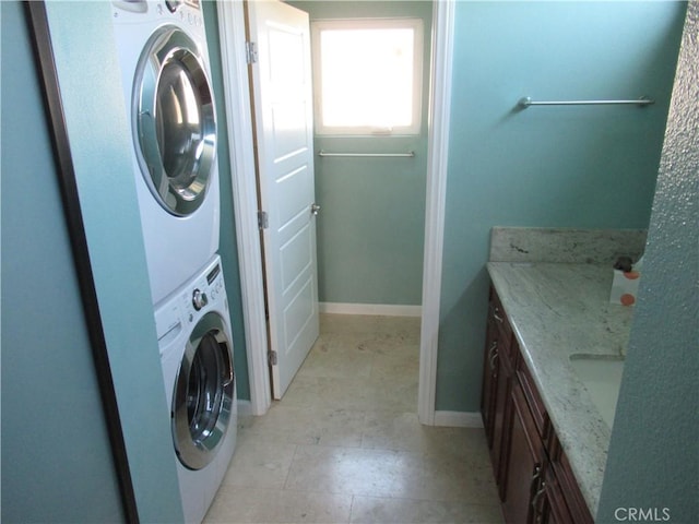 washroom featuring stacked washer / drying machine, laundry area, and baseboards