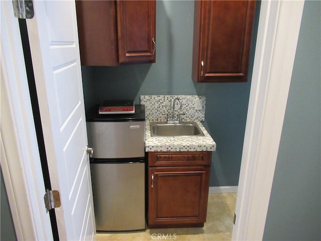 kitchen featuring tasteful backsplash, light countertops, freestanding refrigerator, a sink, and baseboards