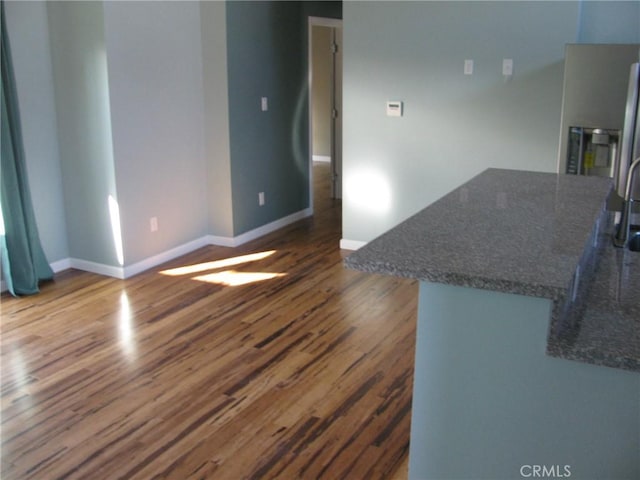 kitchen featuring dark stone countertops, wood finished floors, a center island, and baseboards