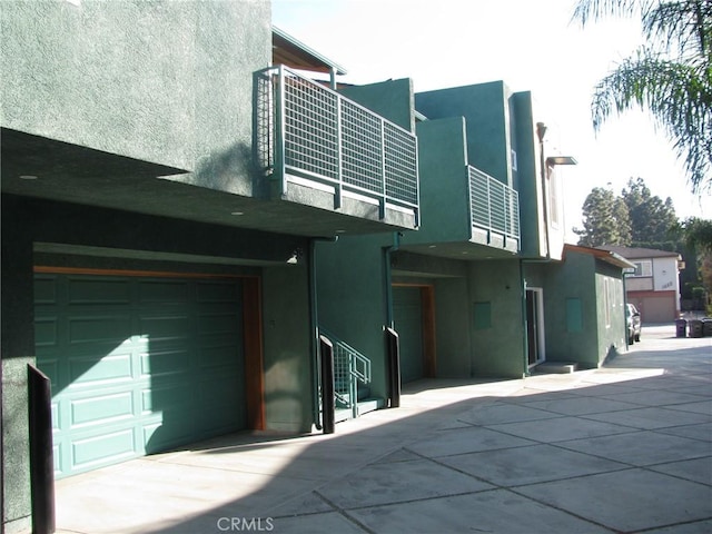 back of property featuring an attached garage, a balcony, and stucco siding