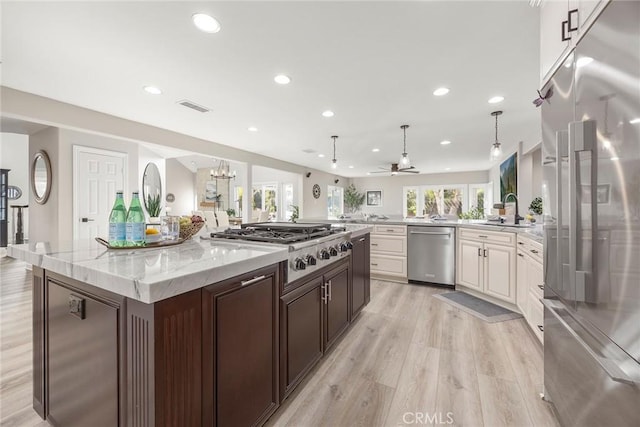 kitchen with stainless steel appliances, a sink, visible vents, light wood-style floors, and light stone countertops