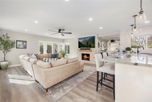 living area featuring recessed lighting, a ceiling fan, light wood-type flooring, a warm lit fireplace, and baseboards