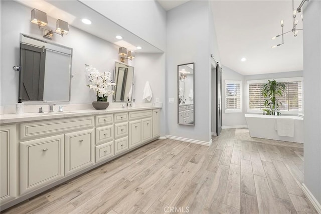 full bath featuring double vanity, a sink, a freestanding bath, and wood finished floors