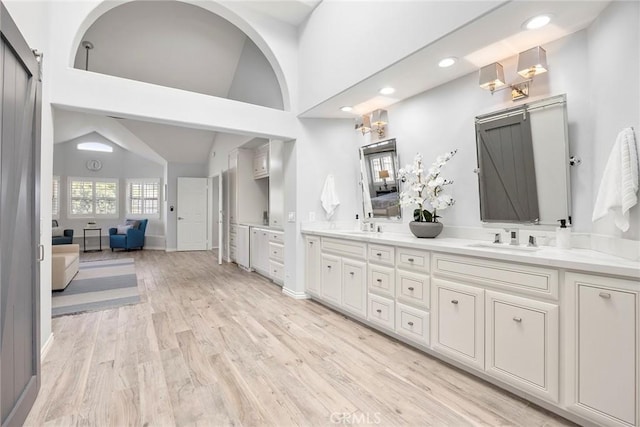 ensuite bathroom featuring a sink, vaulted ceiling, connected bathroom, and wood finished floors