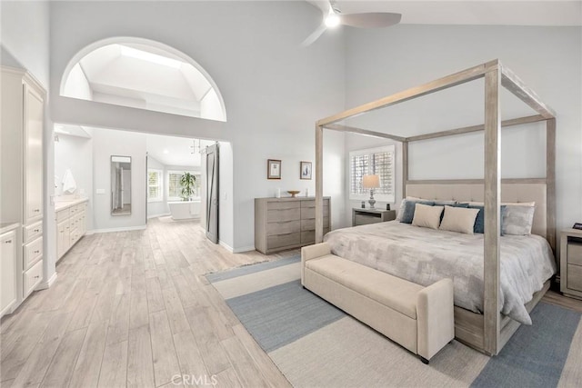 bedroom featuring light wood-style floors, a ceiling fan, connected bathroom, high vaulted ceiling, and baseboards