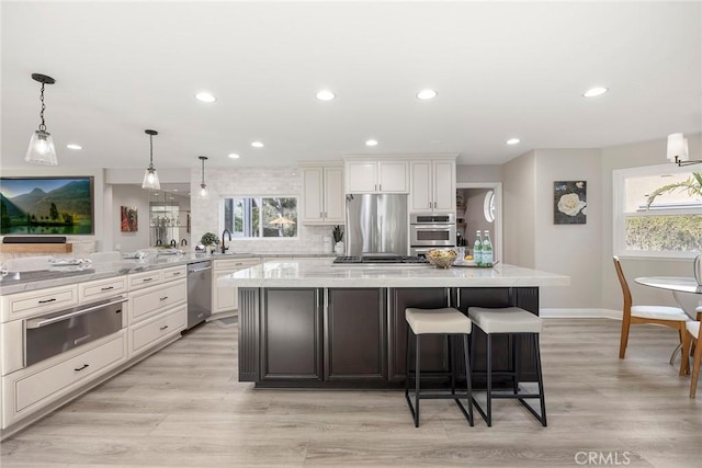 kitchen featuring a warming drawer, stainless steel appliances, backsplash, light wood-style flooring, and a sink