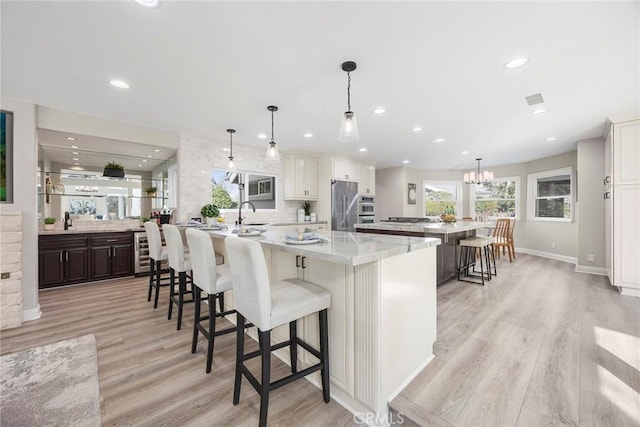 kitchen featuring beverage cooler, stainless steel refrigerator, light wood finished floors, a kitchen bar, and a large island with sink