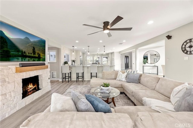 living area with recessed lighting, a fireplace, ceiling fan, and light wood-style flooring