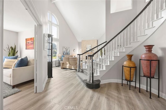 entrance foyer with stairs, high vaulted ceiling, baseboards, and wood finished floors