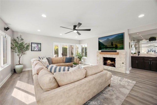 living room featuring a stone fireplace, light wood-style flooring, recessed lighting, a ceiling fan, and baseboards