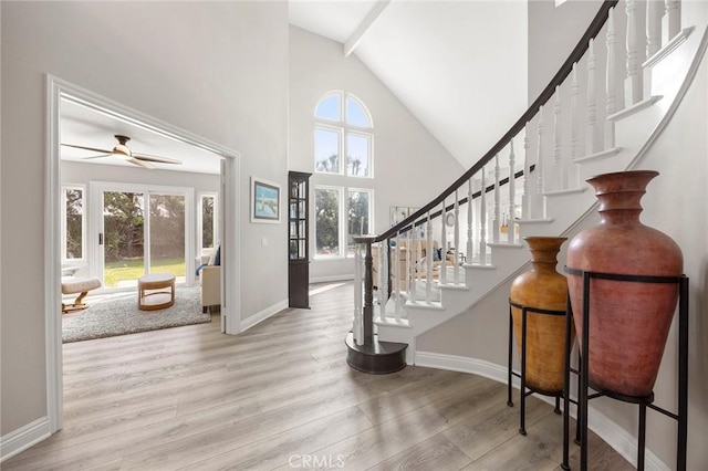 foyer entrance with baseboards, a ceiling fan, wood finished floors, stairs, and high vaulted ceiling