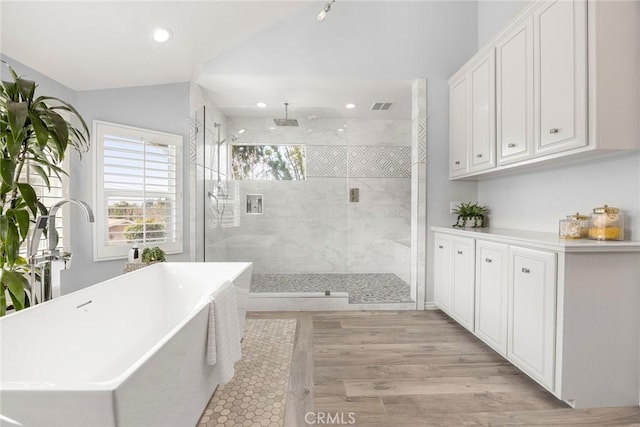 bathroom featuring wood finished floors, visible vents, vaulted ceiling, a soaking tub, and a tile shower