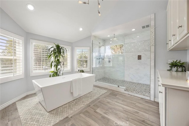 bathroom featuring a soaking tub, vaulted ceiling, a tile shower, and wood finished floors