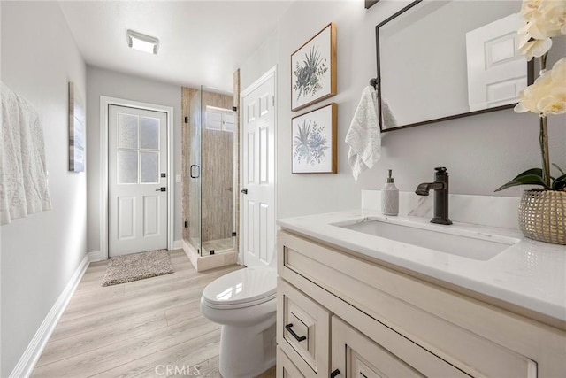 bathroom featuring toilet, wood finished floors, vanity, baseboards, and a stall shower