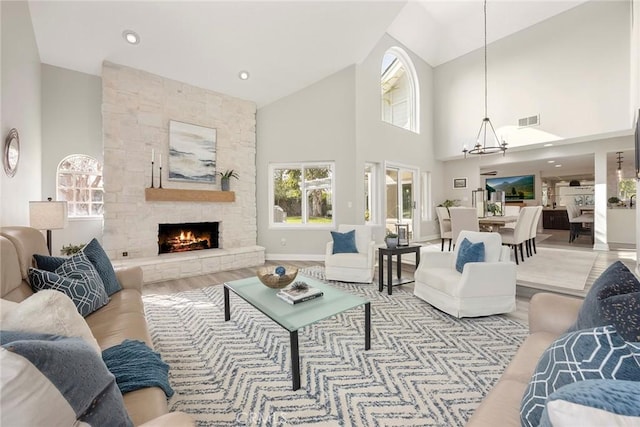 living room with a chandelier, a fireplace, wood finished floors, a towering ceiling, and visible vents