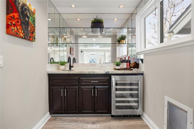 bar with beverage cooler, light wood finished floors, indoor wet bar, and a sink