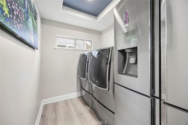 clothes washing area with laundry area, washing machine and dryer, baseboards, and wood finished floors