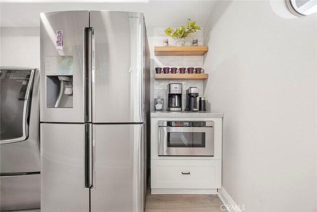 kitchen with light countertops, appliances with stainless steel finishes, light wood-type flooring, open shelves, and tasteful backsplash