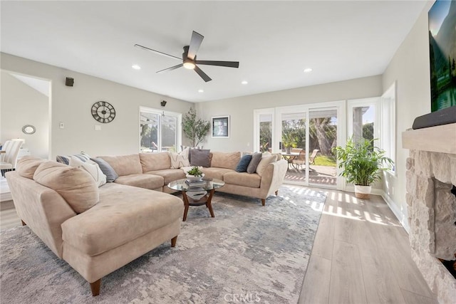 living room featuring a stone fireplace, wood finished floors, a ceiling fan, and recessed lighting