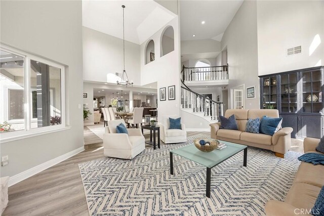 living room featuring wood finished floors, visible vents, baseboards, stairs, and an inviting chandelier