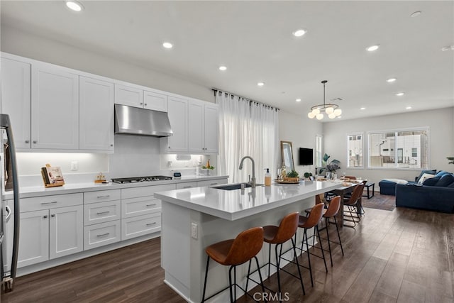 kitchen with under cabinet range hood, dark wood-type flooring, a sink, gas stovetop, and open floor plan