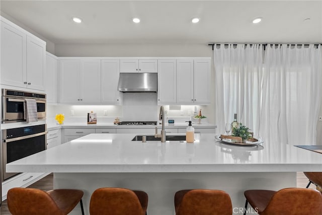 kitchen with under cabinet range hood, a kitchen bar, light countertops, and a sink