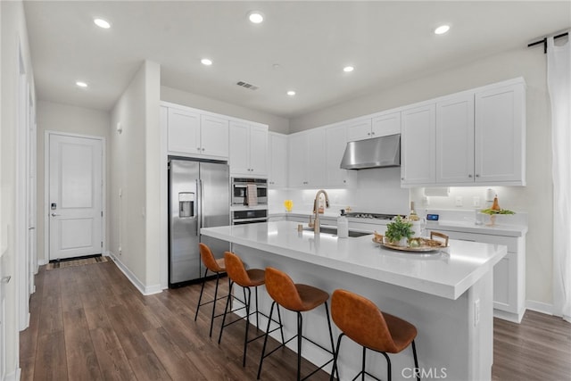 kitchen featuring visible vents, appliances with stainless steel finishes, white cabinetry, under cabinet range hood, and a kitchen bar