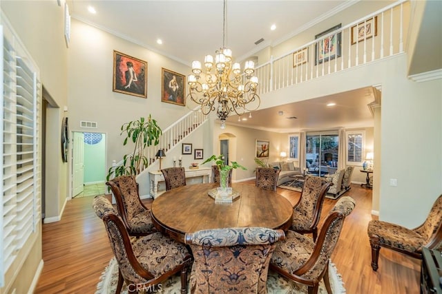 dining space featuring stairway, a high ceiling, crown molding, light wood-style floors, and a chandelier